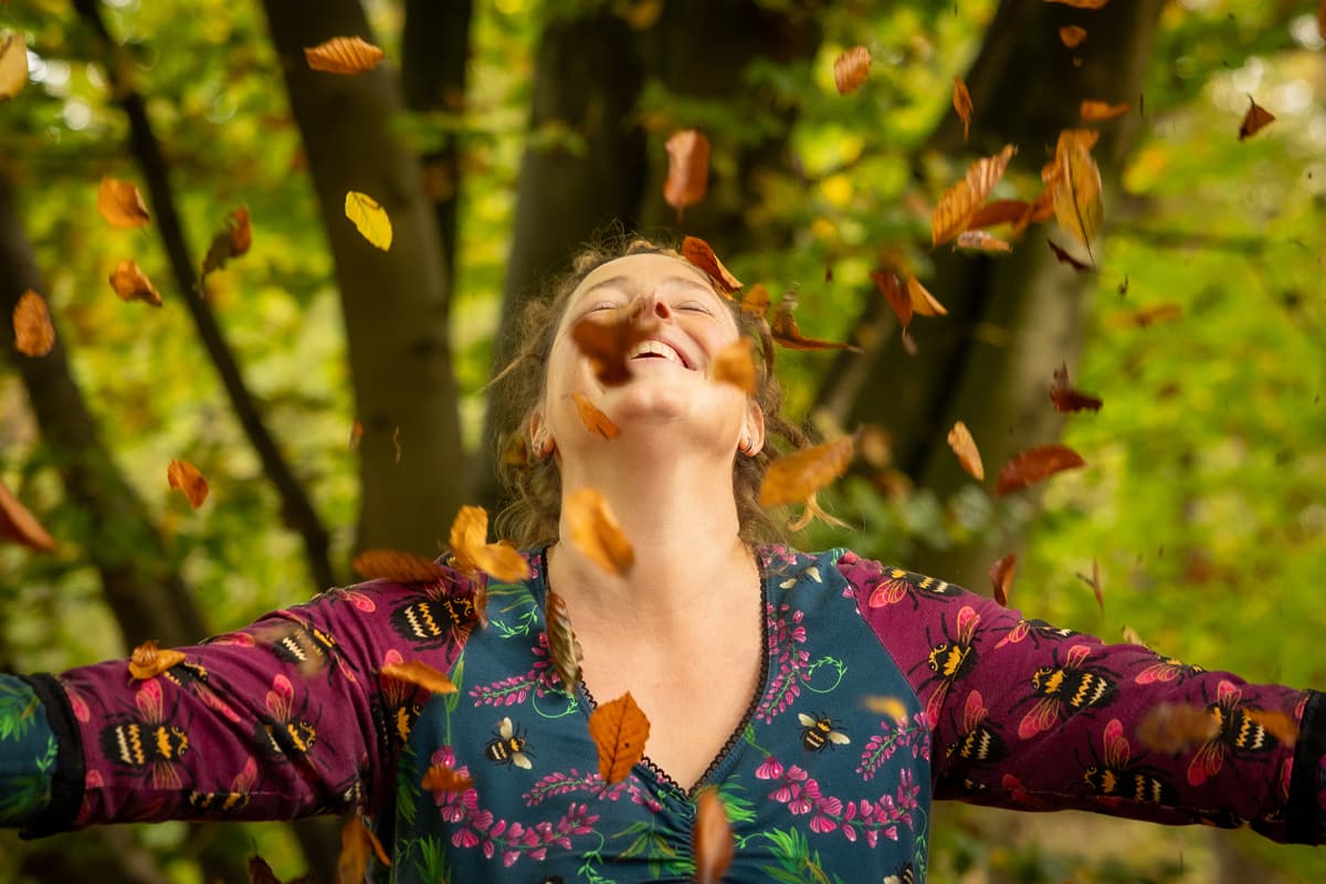 Inge gooit lachend met wijd gespreide armen herfstbladeren in de lucht