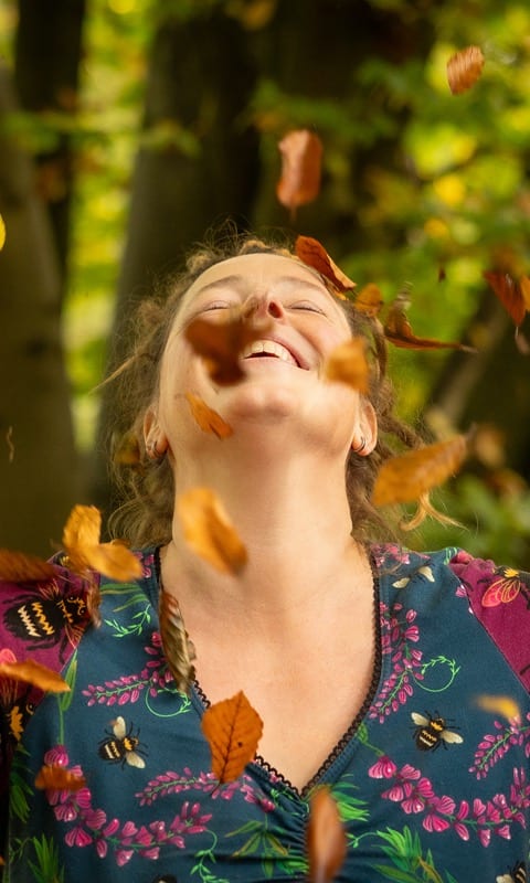 Inge gooit lachend met wijd gespreide armen herfstbladeren in de lucht