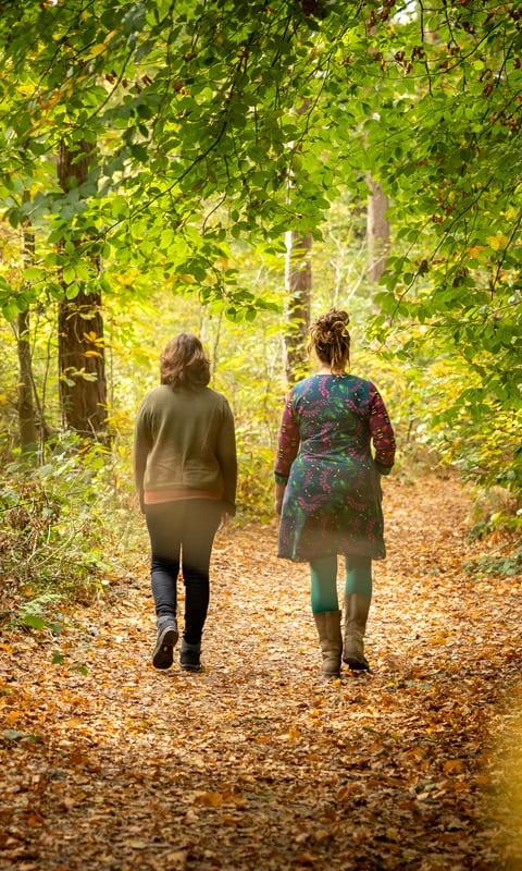 Twee vrouwen wandelen samen over een bospad vol herfstbladeren