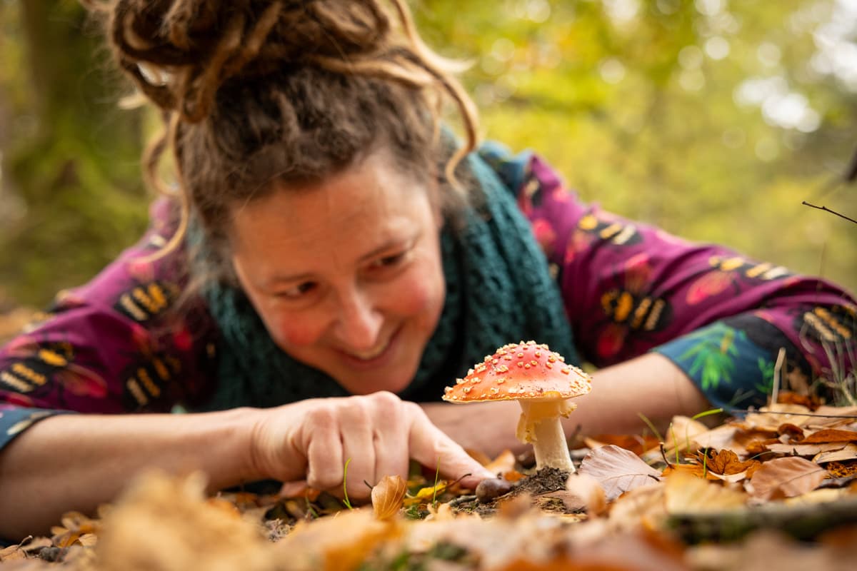 Inge ligt op haar buik in het bos en bekijkt lachend een rode vliegenzwam