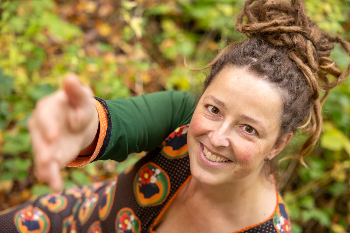 Inge kijkt lachend omhoog naar de camera en steekt haar hand uit
